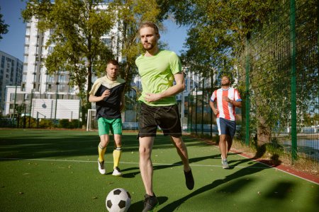 Photo for Sportsmen team playing football on field enjoying active time at countryside. Male hobby, competitive sports game - Royalty Free Image