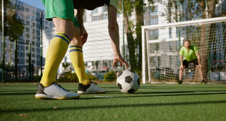 Photo for Football player going to hit soccer ball to score goal into gate defended by goalkeeper. Active summer holiday outdoor and sport match between friends - Royalty Free Image