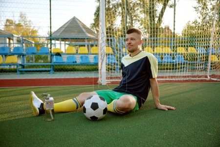 Photo for Young sportive man relaxing after soccer game training. Goalkeeper waiting for team and start second half of football match - Royalty Free Image