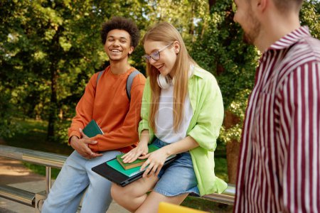 Photo for Confident smiling university students chatting together while taking rest at outdoor campus park. Nice conversation of international people group - Royalty Free Image