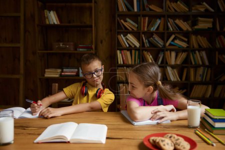 Foto de El astuto hermano quiere copiar la tarea de la hermana mientras los niños estudian juntos en casa. Concepto educativo - Imagen libre de derechos