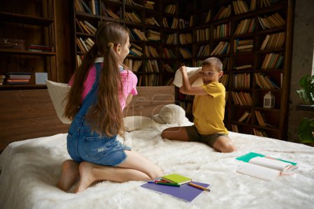 Photo for Cute brother and sister fighting pillows during break in education process. Schoolchildren leisure activity and homeschooling concept - Royalty Free Image