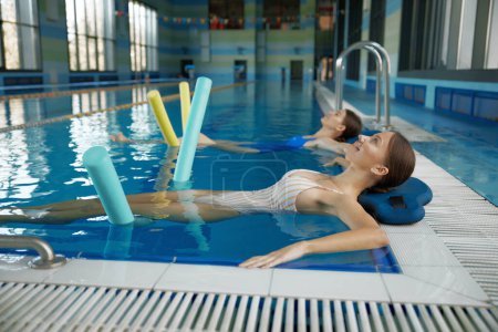 Foto de Dos mujeres haciendo ejercicio relajante con fideos después de la lección de entrenamiento en la piscina. Clase de deportes acuáticos en el centro acuático de ocio - Imagen libre de derechos