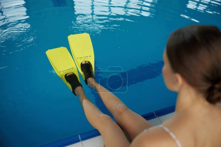 Téléchargez les photos : Gros plan jambes de nageuses portant des palmes au-dessus de la surface de l'eau dans la piscine. Cours de natation et activités de sports nautiques pour plongeurs - en image libre de droit