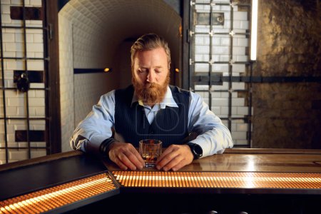 Foto de Retrato de un hombre elegante y considerado mirando un vaso de whisky. Concepto de consumo de alcohol - Imagen libre de derechos