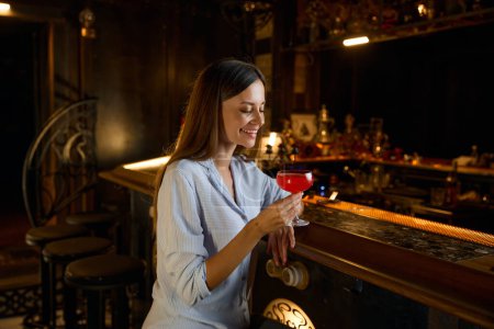 Foto de Feliz mujer sonriente bebiendo cóctel y descansando en el bar. Actividad de ocio por la noche - Imagen libre de derechos