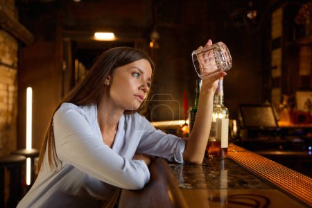 Photo for Drunk young woman looking into empty glass sitting at bar counter. Worried pensive female suffering from alcoholic addiction feeling depressed and burnout - Royalty Free Image