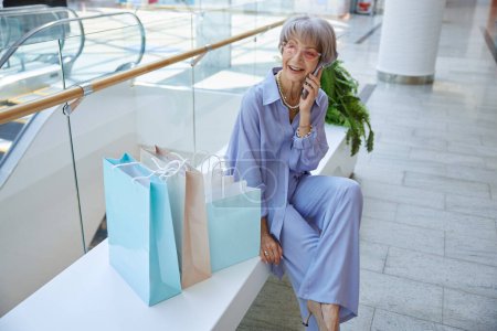 Téléchargez les photos : Femme âgée souriante se détendre après avoir fait du shopping parler par téléphone avec un mari aimant. Bon concept de retraite - en image libre de droit