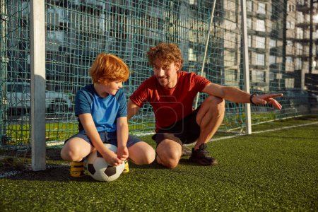 Photo for Portrait of happy father and little son standing near football gate. Family playing soccer on outdoor field - Royalty Free Image