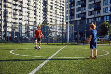 Foto de Padre e hijo jugando entrenamiento de fútbol en el campo de fútbol durante el soleado día de verano. Familia fin de semana actividad deportiva - Imagen libre de derechos