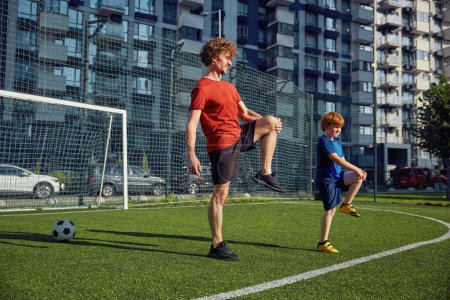 Foto de Padre e hijo deportivo haciendo ejercicio físico y calentando piernas antes del entrenamiento de fútbol en el estadio de la ciudad - Imagen libre de derechos