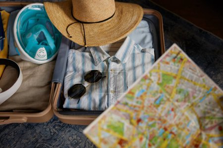 Téléchargez les photos : Valise de voyage ouverte avec vêtements et carte papier sélective. Temps pour le voyage d'été et aller vacances concept - en image libre de droit