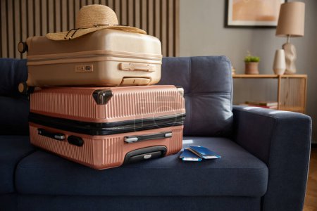 Photo for Stacked travel suitcase with straw beach hat, sunglasses and flight document on home leather sofa. Booking travel, summer vacation and resort tour preparation concept - Royalty Free Image