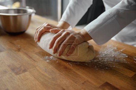 Foto de Mujer panadera con uniforme amasando masa para preparar pasteles o pan en la cocina. Concepto de panadería - Imagen libre de derechos