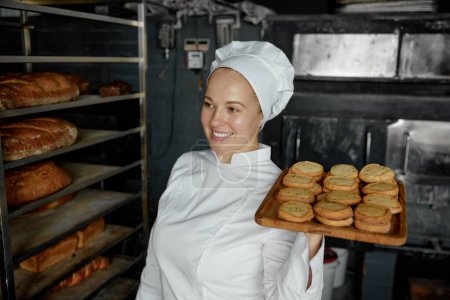 Téléchargez les photos : Femme chef avec plateau d'appétit délicieuse pâtisserie debout à la cuisine de boulangerie. Préparation de biscuits à l'avoine - en image libre de droit