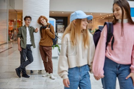Photo for Happy recreation time at big supermarket store center. Boys meeting girls from their school while spending time at mall - Royalty Free Image