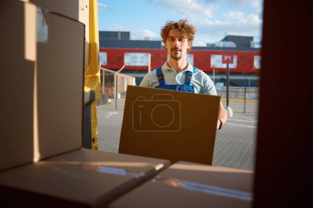 Photo for Warehouse worker in uniform loading van preparing parcel box for delivery. Online goods shopping service with customer order free shipment - Royalty Free Image