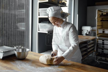 Photo for Happy smiling woman baker shaping dough for cooking bread, pizza or pastry. Professional bakery small business - Royalty Free Image