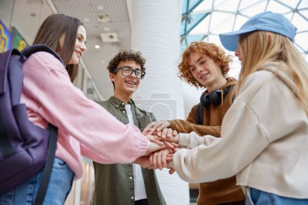 Photo for Teenagers friends standing in circle putting hands together while spending time at shopping mall. Friendship, teambuilding and support - Royalty Free Image