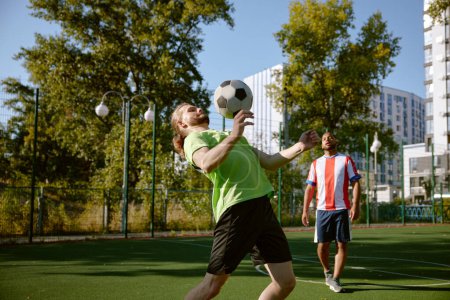 Photo for Male football player hitting ball with his chest training at street soccer field. Outdoor sport hobby activity for adult people - Royalty Free Image