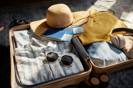 Photo for Suitcase packed with clothes, hat and personal belongings for travel. Male and female luggage bag with vacation stuff kit - Royalty Free Image