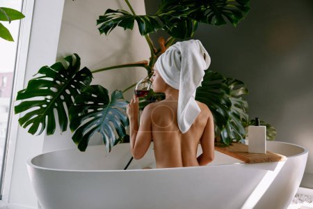 Téléchargez les photos : Belle femme prenant bain dans la salle de bain avec un verre de vin. Procédure Spa, soins de la peau et du corps à domicile, relaxation et bien-être - en image libre de droit