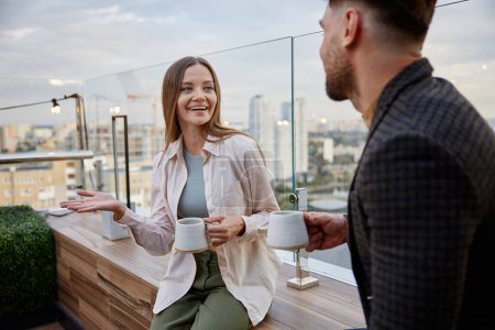 Photo for Man and woman coworkers having nice conversation sharing ideas emotionally speaking at balcony. Freelancers team taking coffee break during workday in office - Royalty Free Image
