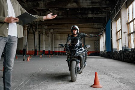 Foto de Estudiante masculino aprendiendo a conducir motocicleta con una mano. Lección con instructor en la escuela de motociclismo - Imagen libre de derechos