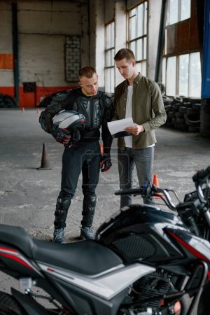 Foto de Estudiante de motociclista e instructor mirando la lista de exámenes de prueba de verificación de errores o la comprensión de los matices de conducción a alta velocidad - Imagen libre de derechos