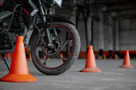 Photo for Closeup view on wheel of training motorcycle parked between traffic road cone at driving school motordrome. Professional education class for motorbike drivers - Royalty Free Image