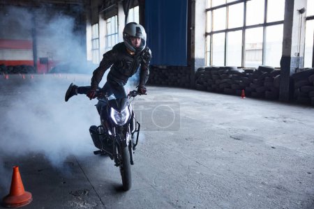 Téléchargez les photos : Cavalier faisant cascade difficile et dangereuse sur sa moto chevauchant rapidement à l'école de conduite moto - en image libre de droit