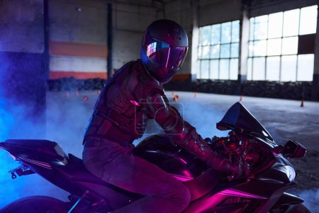 Photo for Portrait of motor biker wearing protective gear and helmet in neon light. Driving school motordrome for training - Royalty Free Image