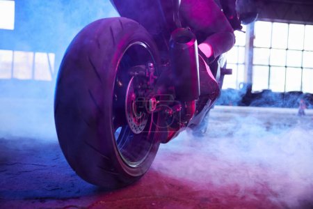 Photo for Closeup sport motorcycle wheel view from back in neon light and smoke. Street racing training at driving school motordrome for practice - Royalty Free Image