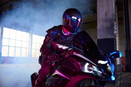 Photo for Portrait of motor biker wearing protective suit and helmet headset driving sport motorcycle in neon light and smoke. Indoor motordrome for speed riding practice - Royalty Free Image