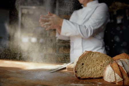 Photo for Female chef hands clapping in cloud of powdery flour over table freeze motion. Culinary process - Royalty Free Image