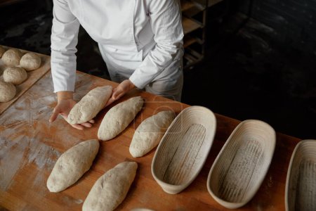 Téléchargez les photos : Baker mains préparer la pâte à pain formé pour l'étanchéité à la boulangerie. Processus de cuisson des baguettes - en image libre de droit