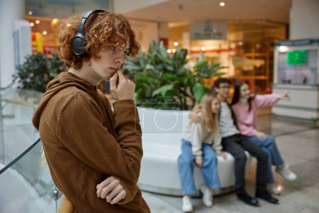 Photo for Portrait of sad serious teenager guy wearing headphones alone at shopping mall. Upset tense young man looking at camera experiencing problems and misunderstanding - Royalty Free Image