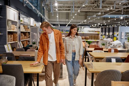 Photo for Positive loving couple testing new furniture for dining room at home furnishing store department. Cheerful man and woman buyers having fun during shopping - Royalty Free Image