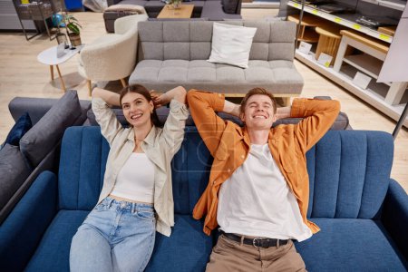 Photo for Relaxed man and woman couple sitting on sofa testing comfort of furniture. Shopping at furnishing showroom - Royalty Free Image