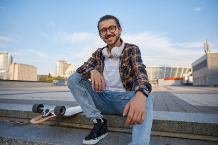 Téléchargez les photos : Cool étudiant gars avec longboard repos sur les escaliers de l'université bâtiment urbain. Skateboard comme moyen de transport en ville - en image libre de droit