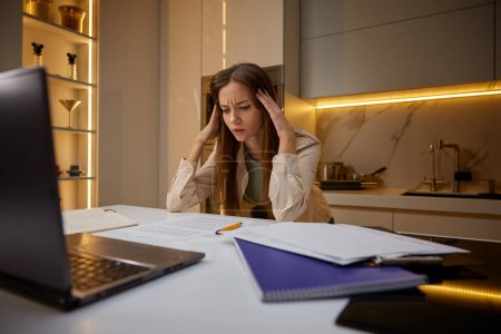 Photo for Overwhelmed woman touching head in panic sitting front of laptop at home. Frustrated shocked millennial woman feeling tired and exhausted, suffering from strong headache from problem - Royalty Free Image