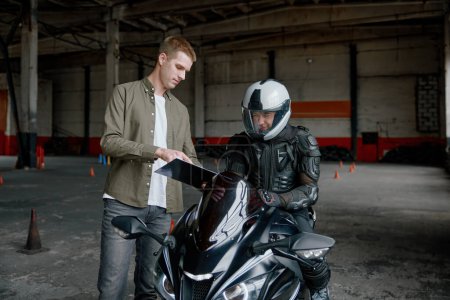 Photo for Motorcyclist passing driving exam at private school to get license. Teacher explaining traffic rules and pointing at mistake of racer during riding - Royalty Free Image