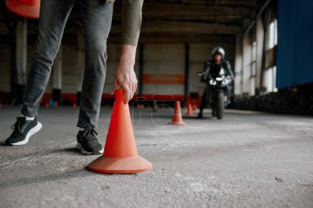 Motorbike driving school lesson with instructor putting cone on track front of student. Indoor motodrome training center