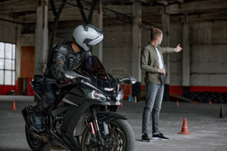 Téléchargez les photos : Homme motocycliste apprendre à faire du vélo à l'école privée manœuvrant entre les cônes à moto intérieure - en image libre de droit