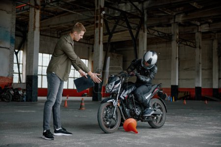 Foto de Hombre motociclista cometer error tocando cono durante la clase de equitación personal en la escuela. Examen del permiso de conducción - Imagen libre de derechos