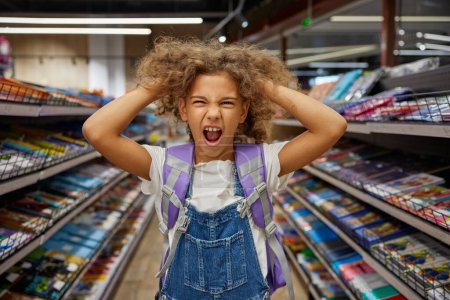 Photo for Stressed girl child feeling crazy during busy shopping at stationery shop. Mad female kid tearing hair on head screaming loudly portrait. Children emotion, purchases and back to school concept - Royalty Free Image