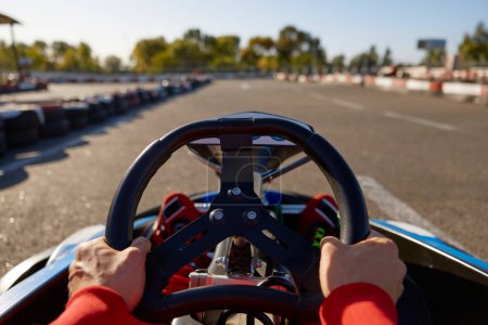 Téléchargez les photos : Gros plan go-kart coureur voiture de sport de conduite avec l'accent sur les mains tenant volant. Poursuite récréative, concept de course de vitesse de chariot - en image libre de droit