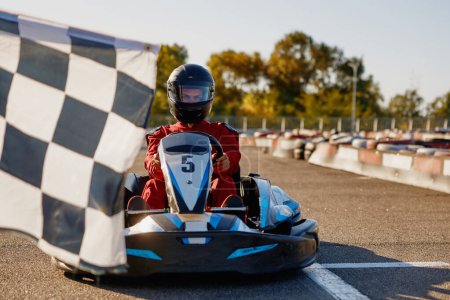 Photo for Go-kart driver crossing at finish line moving to checkered racing flag. Active battle win for first place in extreme auto sports championship - Royalty Free Image