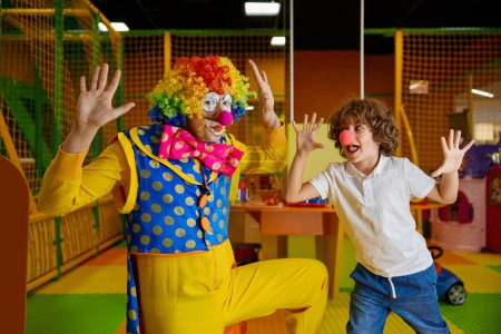 Photo for Funny clown animator and boy fooling around playing at indoor playroom of modern entertainment center for children - Royalty Free Image