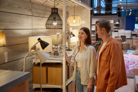 Photo for Young family couple choosing chandelier in building shop center. Handsome man and attractive woman lovers selecting exclusive electric lightning equipment for their new apartment house at retail store - Royalty Free Image